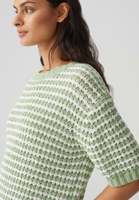 Pull en tricot avec des rayures vertes et blanches alternées, manches courtes, et une finition texturée avec un col et des poignets côtelés.