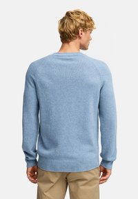 Lyseblå genser laget av myk strikket stoff, med klassisk passform, raglanermer og ribbestrikkede mansjetter og hem. Glatt tekstur.