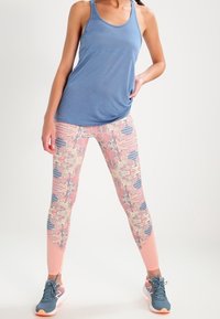 Un débardeur sans manches bleu associé à des leggings colorés et à motif, présentant des designs floraux et rayés, complété par des chaussures de sport grises.