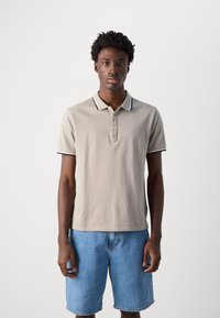 Polo shirt bej dintr-un material texturat, cu o deschidere cu trei nasturi și detalii bleu marin la guler și la mâneci, asociat cu pantaloni scurți din denim.