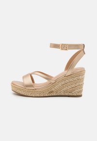 Wedge sandals with a metallic gold leather upper, crisscross straps, and an espadrille-style woven jute platform. Ankle strap with buckle detail.