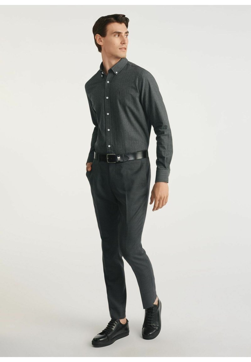 Ciemnoszara koszula zapinana na guziki z kołnierzykiem, zestawiona z pasującymi dopasowanymi spodniami oraz czarnymi trampkami. Gładki materiał, dopasowany fason.