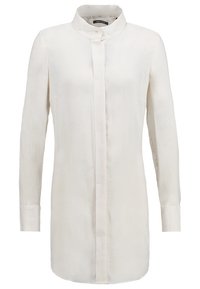 Blouse blanche à manches longues avec col montant et patte de boutonnage dissimulée, conçue pour un look épuré et minimaliste.
