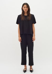 Černý top s krátkým rukávem a volným střihem, v kombinaci s černými kalhotami rovného střihu. Hladká tkanina, minimalistický design a žádné viditelné vzory.
