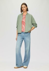 Lichtgroene bomberjack, rood patroon top, ruime lichtblauwe jeans en tan sneakers. Eenvoudig, casual ontwerp met zachte texturen.
