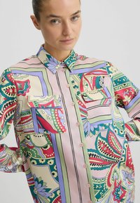 Langarm blouse met knopen in patroonzijde, met een pastel kleurenpalet en ingewikkelde bloemen- en geometrische ontwerpen, twee borstzakken.
