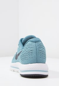 Modré pletené sportovní boty s bílou podrážkou a černým logem swoosh, z pohledu zezadu na bílé ploše.