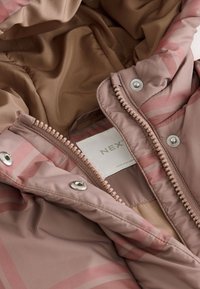 Giacca imbottita di un rosa chiaro con finitura lucida, dotata di fodera con motivo, chiusura a zip e dettagli in metallo. Il tessuto ha una texture liscia.