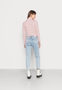 Top de manga longa rosa com padrão de corações vermelhos, combinado com jeans justos azul claro e botas brancas até ao tornozelo com solas pretas.