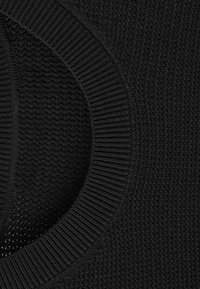 Gros plan sur un tissu noir tricoté avec un col rond côtelé et un motif texturé sur le corps principal du vêtement.