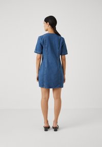 Vestido de ganga com mangas curtas, cor azul clara, corte reto e detalhes de costura mínimos. A bainha está acima do joelho.
