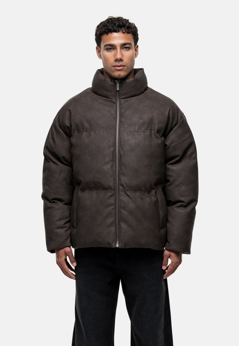 Veste rembourrée marron avec un col montant, fermeture à glissière sur le devant et deux poches latérales. Fabriquée en matériau lisse et texturé avec des détails de couture.