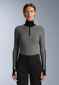 Crna i bijela majica s dugim rukavima i zatvaračem na vratu, s teksturiranim cik-cak uzorkom i crnim rubom. Uparena s prilagođenim crnim hlačama s džepovima.