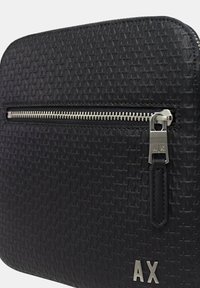 Borsa nera con cerniera dalla superficie texturizzata, caratterizzata da un motivo ripetuto. Finiture in argento per la cerniera e dettaglio del logo nella parte inferiore.
