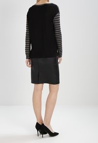 Haut noir à manches longues avec des manches rayées grises, associé à une jupe en cuir noir et des stilettos noirs. Texture lisse, design ajusté.