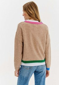 Beżowy sweter z dzianiny z okrągłym dekoltem, z wielokolorowymi prążkowanymi akcentami w różowym, niebieskim i zielonym. Miękka tekstura i luźny krój.