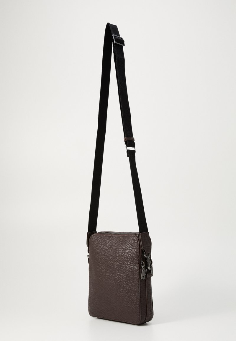 Bolso de cuero marrón texturizado con forma rectangular, correa ajustable negra y herrajes de cremallera en tono plateado. Diseño compacto y funcional.