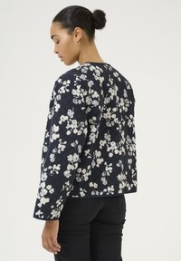 Quilted navy jacket with white floral pattern, round neckline, and long sleeves. Textured fabric with a casual fit and back design.