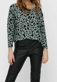 Jasnozielony sweter dzianinowy z czarnym nadrukiem w lamparta, z szerokim dekoltem i długimi rękawami, w połączeniu z czarnymi skórzanymi spodniami.