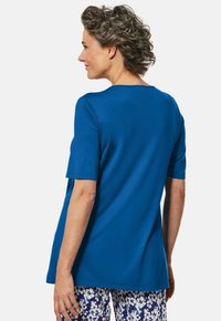 Blaues Kurzarmoberteil in einem lockeren Schnitt. Glattes Jersey-Material mit Rundhalsausschnitt, kombiniert mit gemusterten Hosen mit floralen Designs.