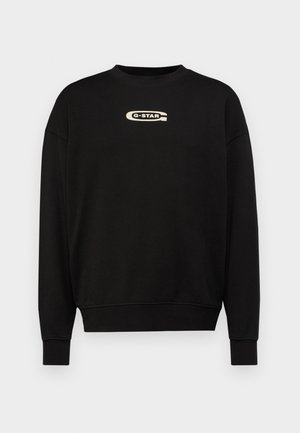 Svart hettegenser med rund hals og senkede skuldre. Har en kontrasterende beige G-STAR-logo over brystet. Ribbestrikkede mansjetter.