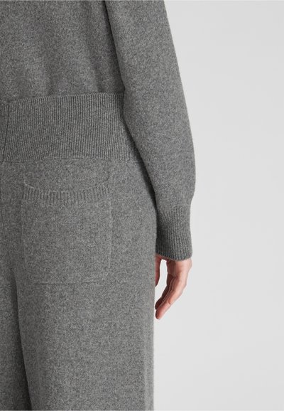 Grauer Strickpullover mit gerippten Bündchen und Saum. Verfügt über eine kleine Patten- Tasche auf der Rückseite. Weicher Stoff, lockere Passform.