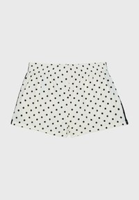 Shorts blancs à taille élastique avec des pois noirs et une bande noire le long des côtés, présentés sur un fond uni.