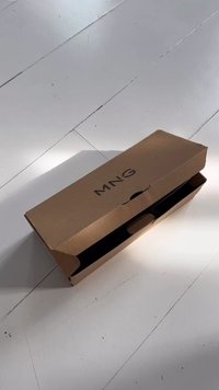 Hnědá kartonová krabice s horním klapkou, která má výřez na rukojeť a vytištěné logo "MNG" v tučném, centrovaném písmu na víku.
