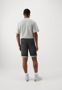 Camiseta gris de manga corta combinada con pantalones cortos de mezclilla oscuros con dobladillos enrollados, bolsillos traseros y zapatillas altas de color azul claro.