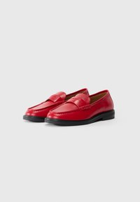 Red leather loafers with a textured seam detail, featuring a smooth finish and a black rubber sole. Classic design with a rounded toe.
