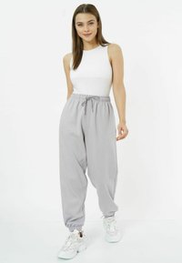 Helle graue Jogginghosen mit elastischem Bund und Bündchen, kombiniert mit einem taillierten weißen Tanktop und weißen Sneakers. Glatte Stofftextur.