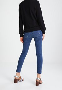 Suéter negro de mangas largas, jeans ajustados azules y sandalias de tacón plateadas. Detalles notables incluyen un escote redondeado y tacones con acentos de madera.