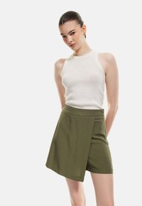 Haut sans manches en tricot blanc et short cache-coeur vert olive. Le haut présente une texture côtelée, tandis que le short est en tissu lisse avec un ourlet droit.