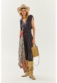 Sivý overal s krátkymi rukávmi, sťahovaným pásom a vzorovanou šatkou. Béžové voľne sedené čižmy, strapcovú kabelku a svetlú čiapku. Neutrálny pozadie.