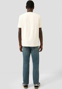 Kremowy t-shirt z krótkim rękawem i okrągłym dekoltem, połączony z jasnoniebieskimi dżinsami. Gładka, płaska tekstura i luźny krój.
