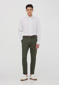 Camicia bianca con bottoni, pantaloni verde oliva, cintura marrone e sneakers bianche con dettagli color nocciola. Tessuto morbido e vestibilità sartoriale.
