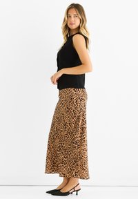 Black sleeveless top paired with a long leopard print skirt in tan and black, complemented by black slingback heels. Smooth textures throughout.
