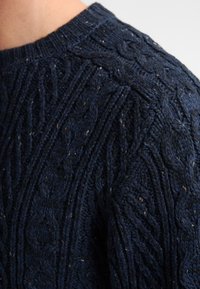 Pulover tricotat bleumarin cu un model texturat de tricotaj în formă de cablu, guler rib și un material moale, gros, cu o textură ușor aspră.