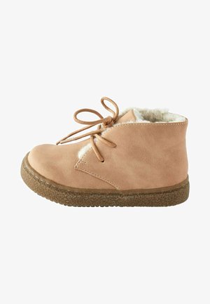 Bottine en suède tan avec fermeture à lacets, doublure pelucheuse et semelle en caoutchouc texturée. Bout rond et détails de couture minimaux.