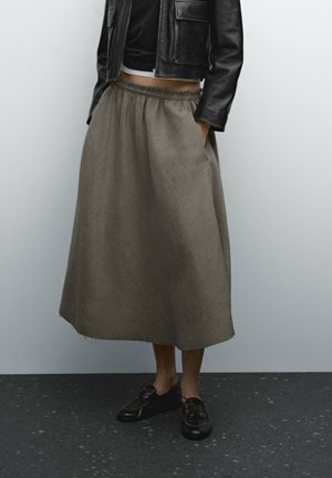 Personne portant une jupe midi marron à carreaux avec poches, une veste courte en cuir noire, un haut noir et des chaussures noires à lacets.