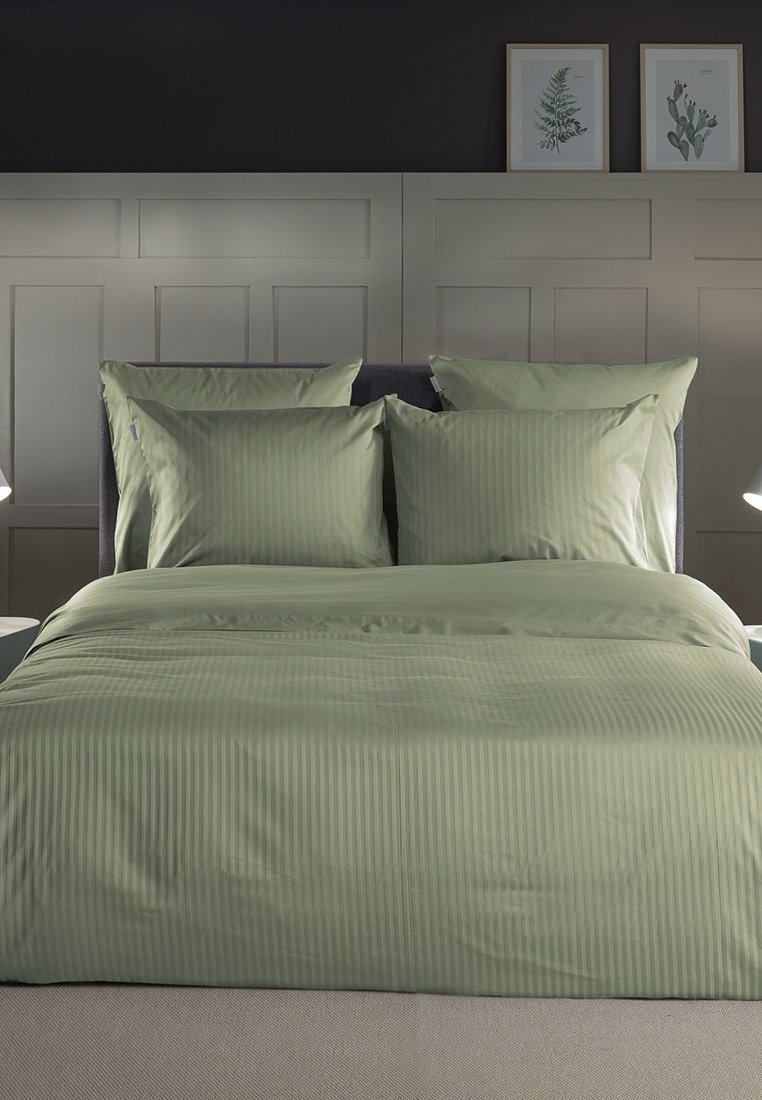 Juego de cama a rayas verdes que incluye un edredón texturizado y dos almohadas a juego sobre una cama. Diseño minimalista sobre un fondo neutro.