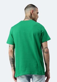 T-shirt in cotone verde con scollatura rotonda classica e maniche corte. Texture liscia, vestibilità comoda, senza motivi o dettagli visibili.