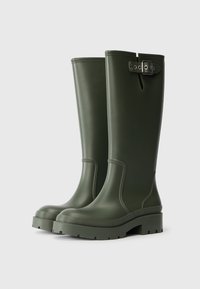 Groene rubberen regenlaarzen met een gladde textuur, hoge schacht, verhoogde zool en gespsluiting bij de bovenrand. Eenduidige kleur met minimale designelementen.