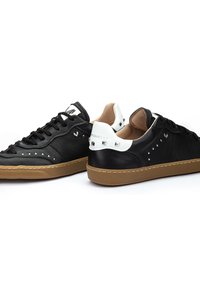 Zapatillas negras de cuero con detalles en blanco, suela de goma, tachuelas decorativas y diseño de corte bajo. Frente con cordones y textura suave.