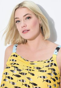Top amarillo con un patrón de peces negro, con tirantes negros y celestes. Tejido suave con un diseño drapeado.