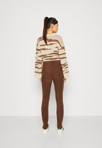 Brune suedette leggings kombinert med en beige stripete strikkegenser. Teksturen er myk, og genseren har en løs passform og vide ermer.