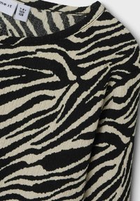 Maglione a strisce zebra nero e crema con texture a coste e scollo rotondo. L'etichetta indica la taglia 7-8 anni.