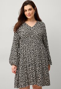Schwarzes Blumenkleid mit langen Ärmeln und V-Ausschnitt, das eine geraffte Taille und eine fließende Silhouette aufweist. Das Muster besteht aus kleinen weißen Blättern.