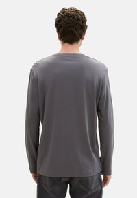 Long-sleeve gray shirt made of soft fabric, featuring a crew neck and a relaxed fit, with minimal stitching details on the shoulders.
