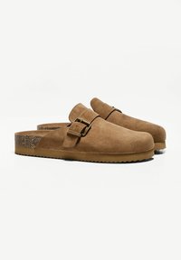 Barna velúr klumpák széles pánttal, sárgaréz csattal és textúrált parafa talppal. Slip-on dizájn jellemzi, valamint bordázott gumitalp.